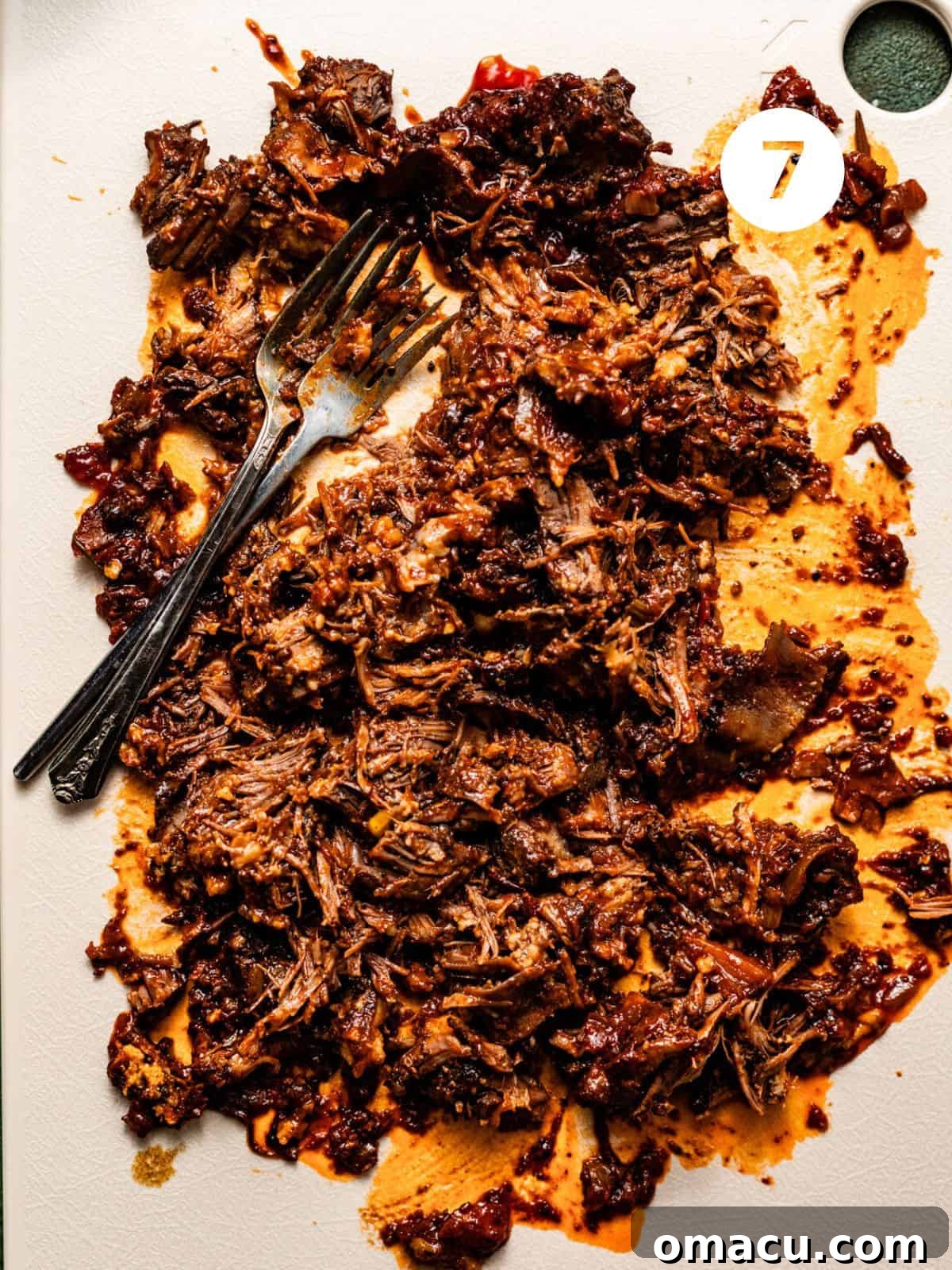 Perfectly shredded short rib meat on a cutting board, ready to be incorporated back into the bolognese sauce.