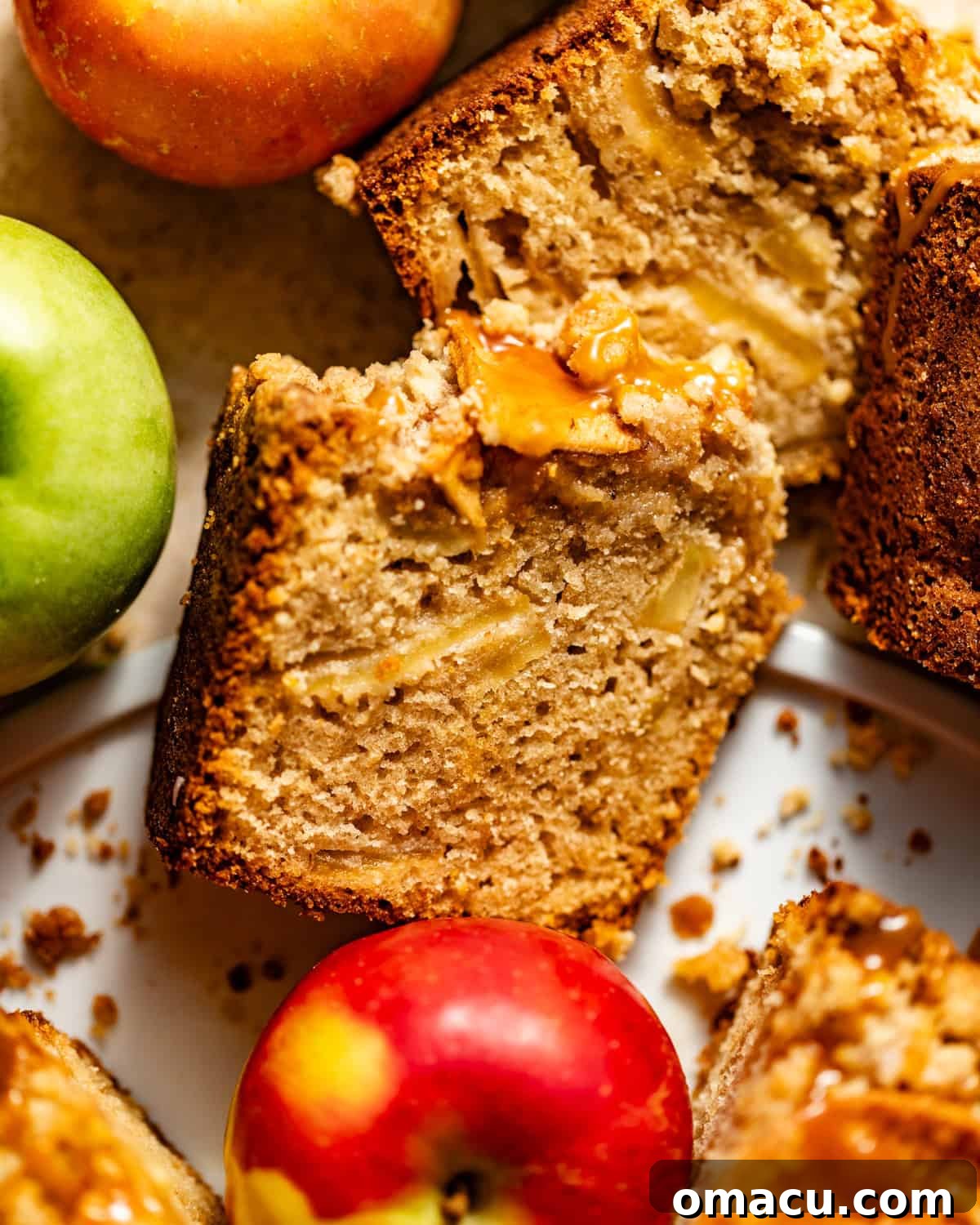 A single slice of fluffy apple crumb cake, generously topped with streusel, resting on a white plate. Fresh apples and crumbs are scattered artistically around the plate.