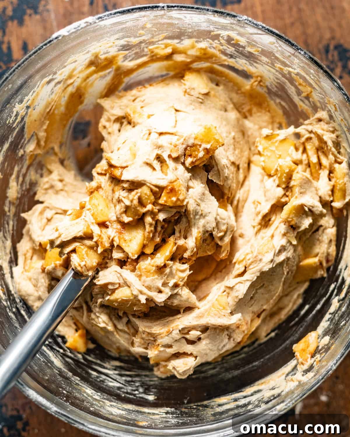 Light brown apple crumb cake batter in a bowl, with vibrant fresh apple slices visibly folded throughout the mixture.