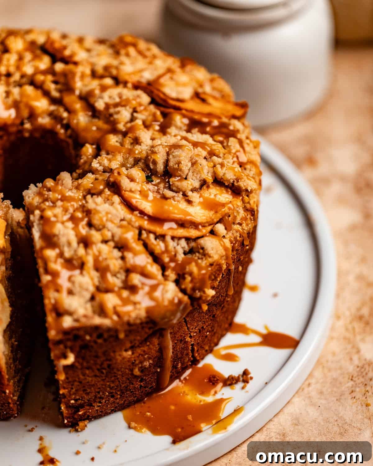 A close-up of a slice of apple crumb cake on a plate, decadently covered with a generous drizzle of homemade salted caramel sauce.