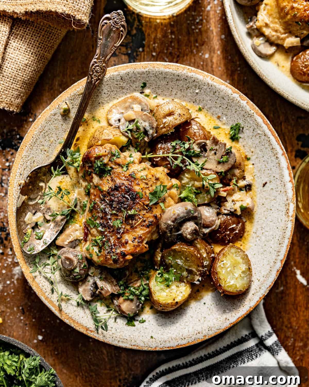 coq au vin blanc on a plate with potatoes and chopped parsley on top. 