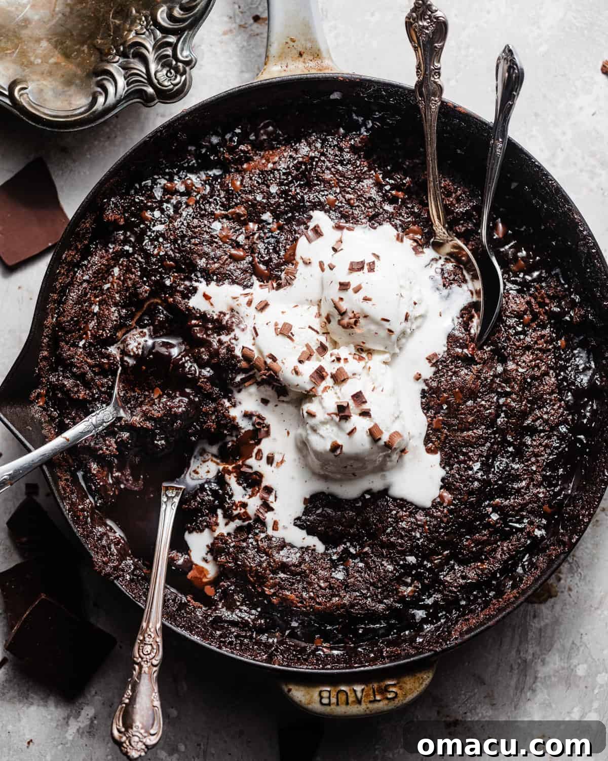 A warm chocolate pudding cake in a cast iron skillet, topped with melting vanilla ice cream and delicate chocolate shavings, ready to be enjoyed.