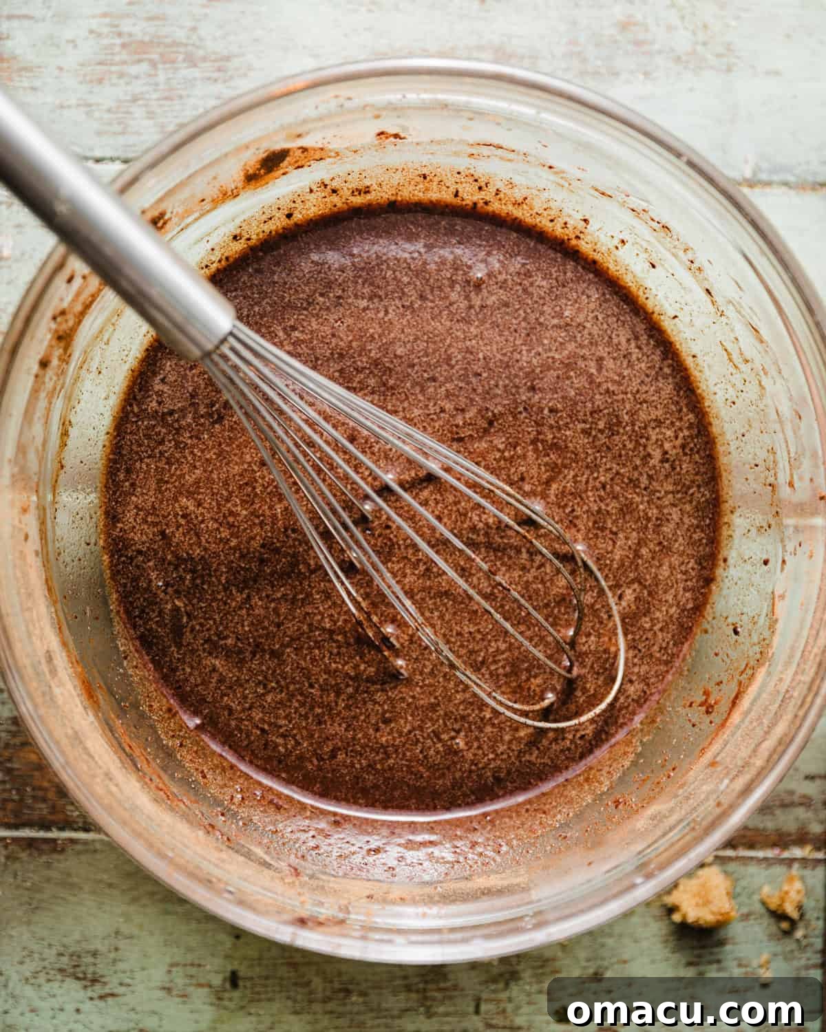 Warming milk, espresso powder, butter, and oil are being whisked together with brown sugar, cocoa powder, and vanilla extract in a mixing bowl for the chocolate cake batter.