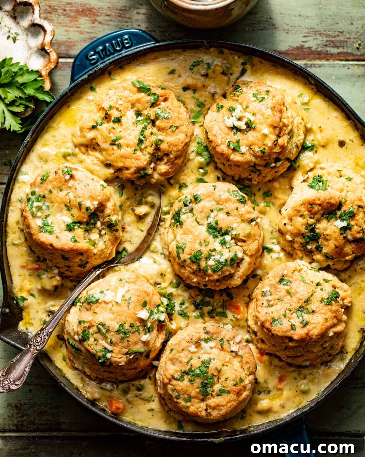 A skillet filled with bubbling chicken pot pie, generously topped with golden-brown cheddar bay biscuits, with a serving spoon resting inside.