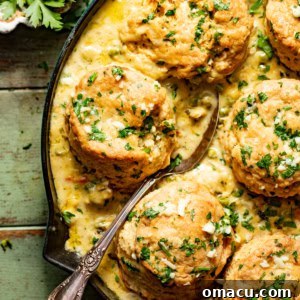chicken pot pie in a skillet topped with cheddar bay biscuits with a spoon.
