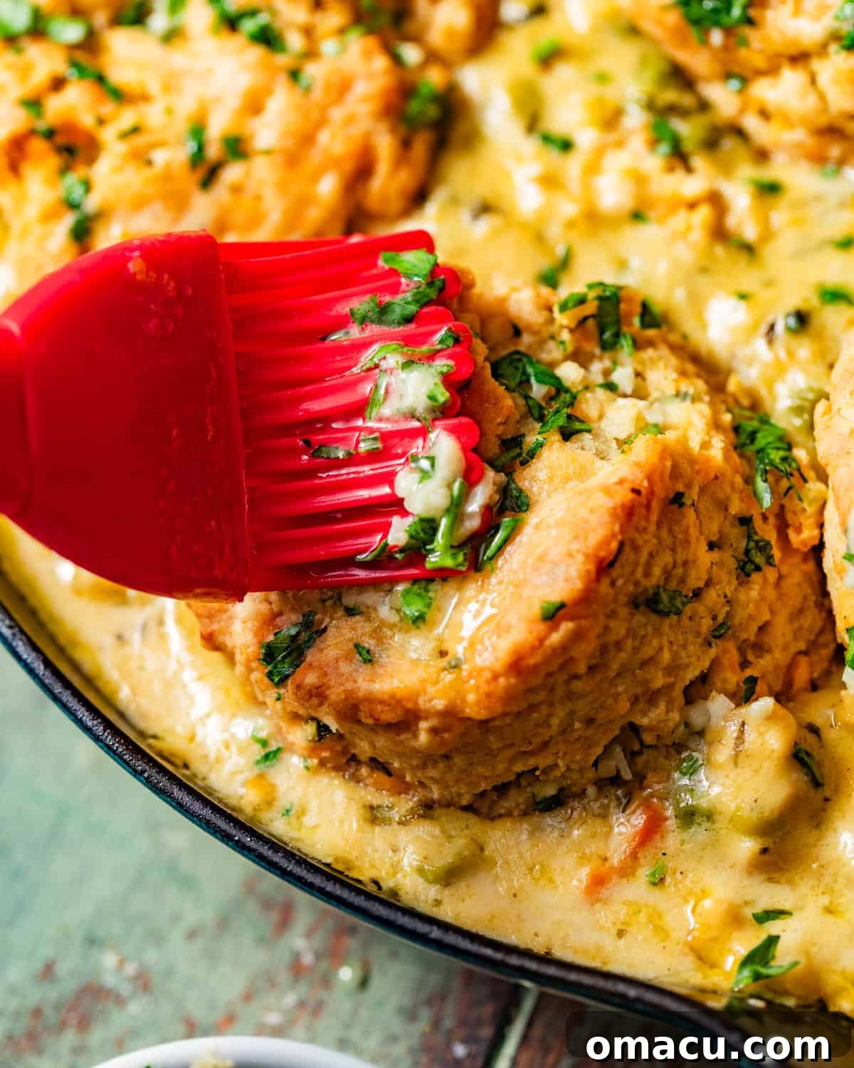 Garlic butter being brushed onto the golden-brown cheddar bay biscuits atop the chicken pot pie.