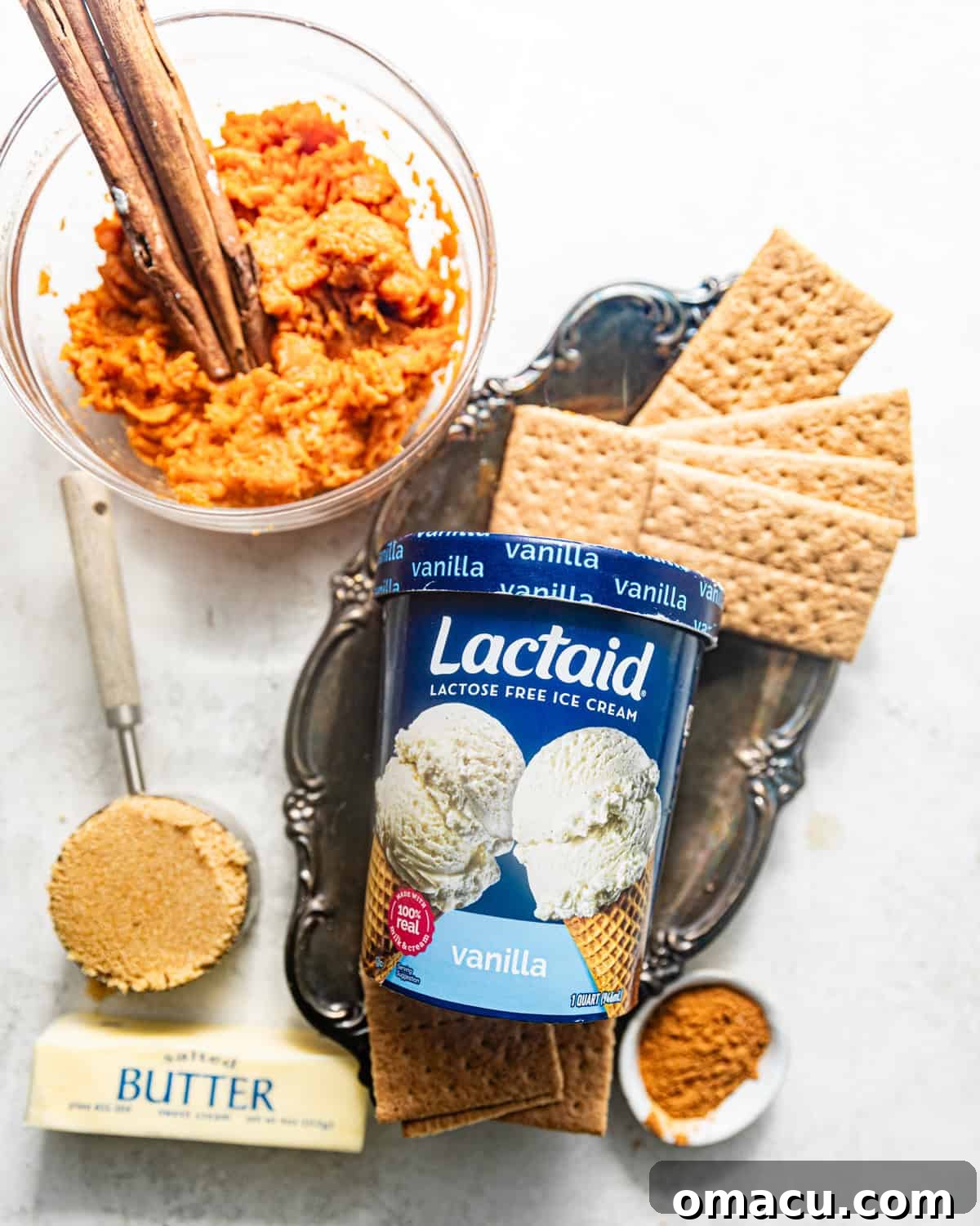 A curated display of ingredients for sweet potato ice cream on a clean white surface, featuring vibrant sweet potatoes, warm cinnamon, earthy nutmeg, rich butter, dark brown sugar, creamy vanilla ice cream, and crunchy graham crackers.