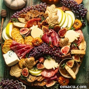 fall charcuterie board on a green wooden surface with pumpkin and a coffee pot around the board.