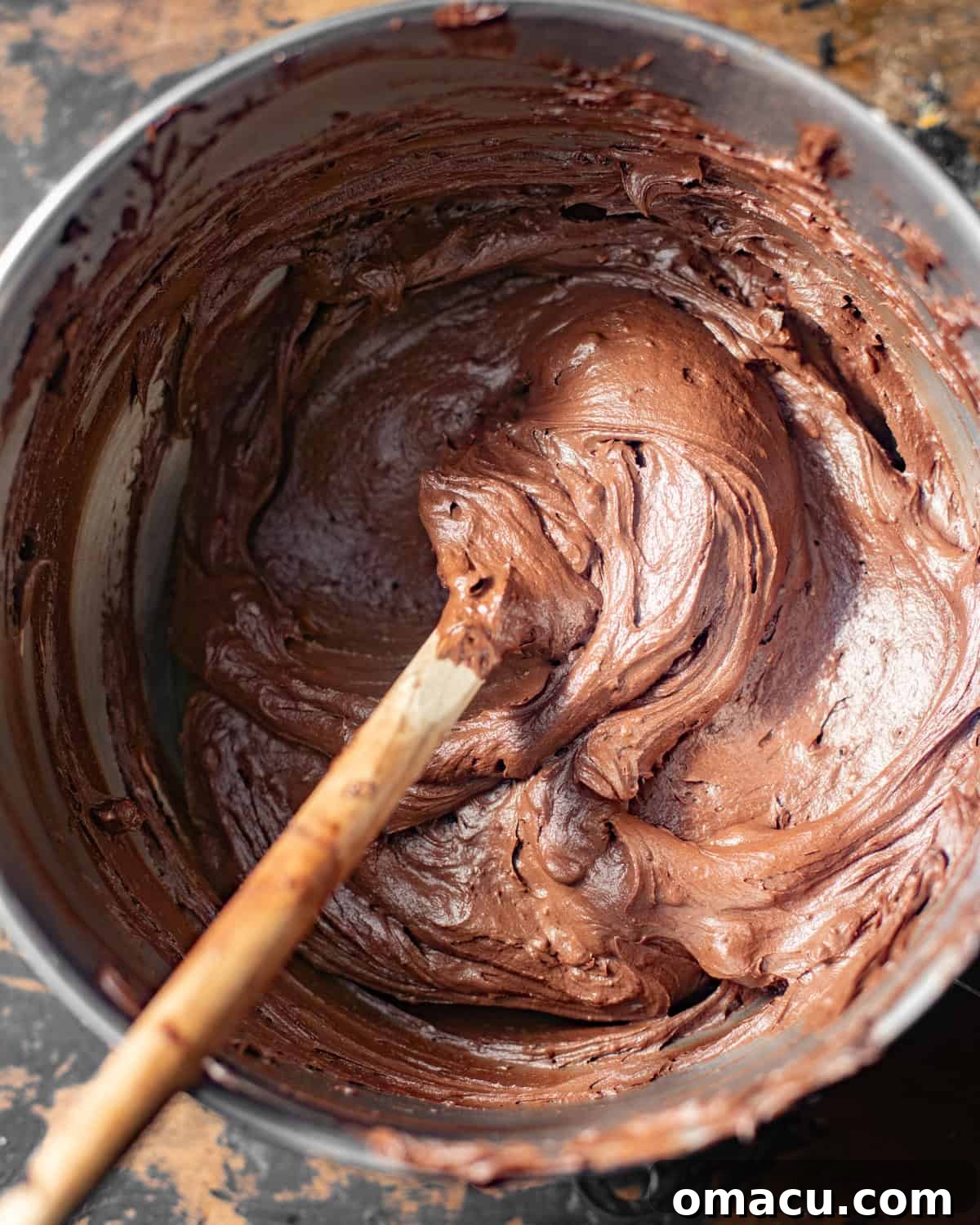 Rich chocolate cream cheese frosting in a stand mixer bowl, being smoothed with a spatula.