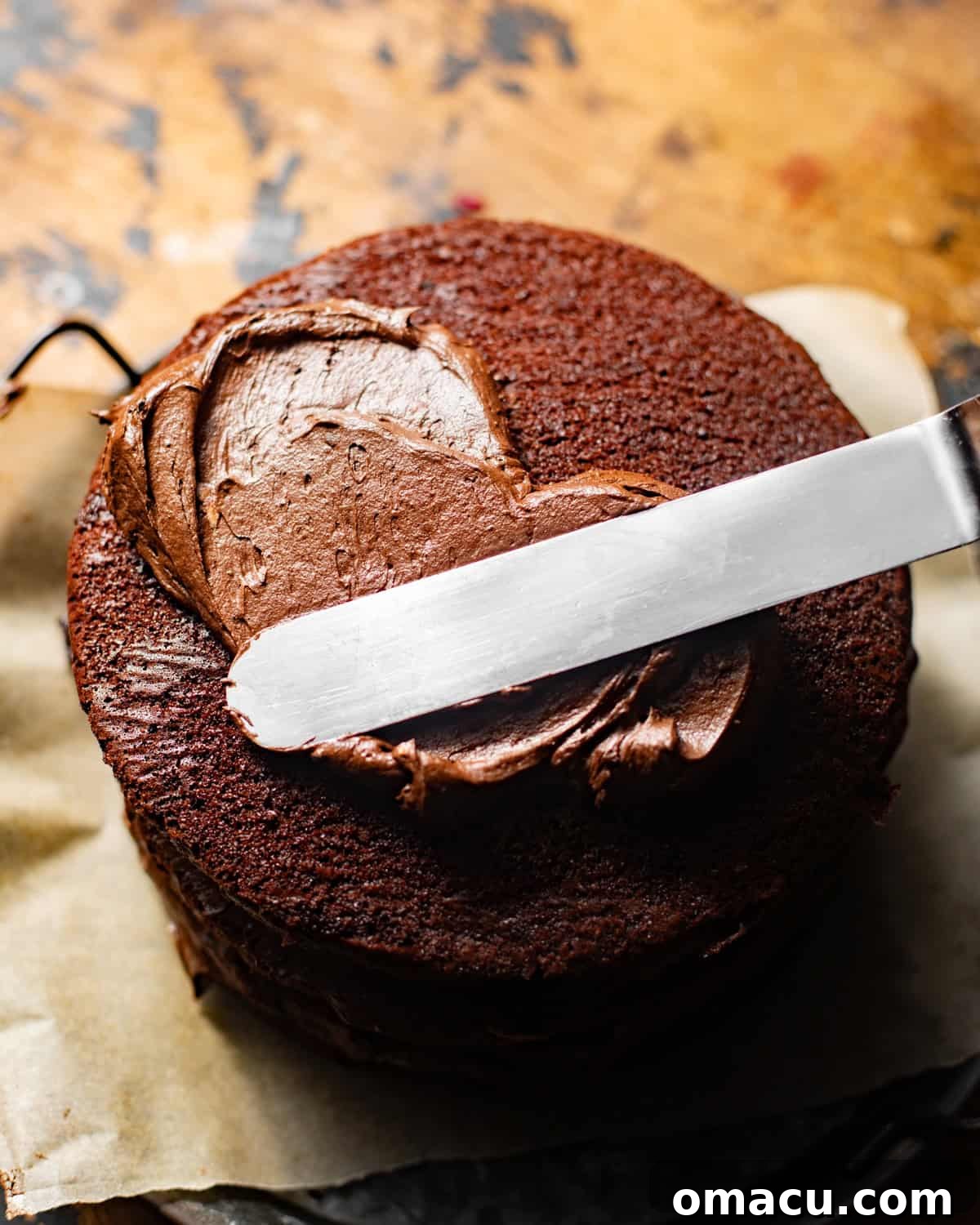 The initial crumb coat being applied to Matilda's chocolate cake on parchment paper, preparing it for the final frosting layer.