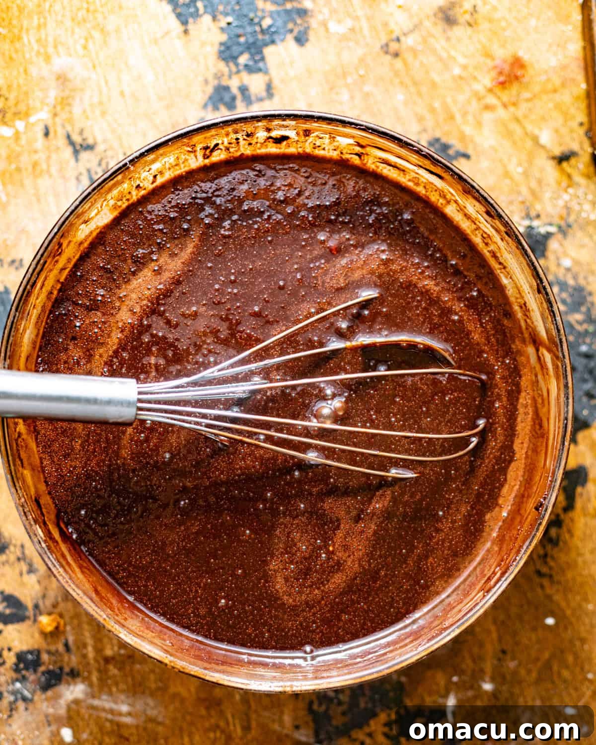 A mixing bowl filled with wet ingredients like cocoa powder, hot milk, coffee, espresso powder, sugars, vegetable oil, and melted butter.