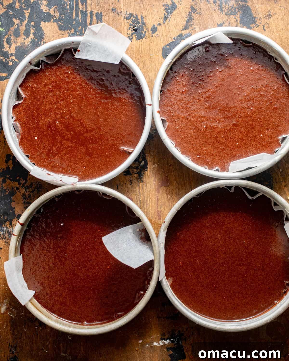 Chocolate cake batter evenly divided into four 8-inch cake pans, ready for the oven.