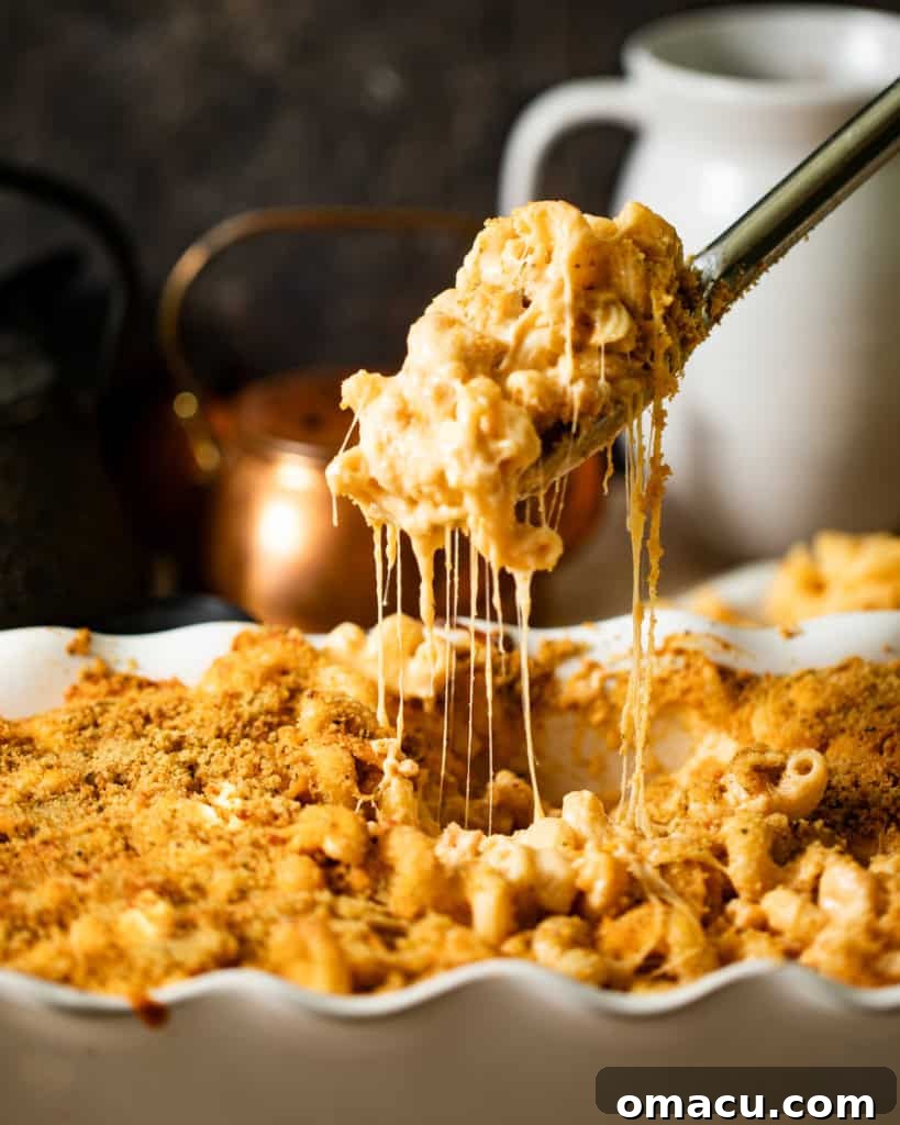 A glorious close-up of baked mac and cheese in a baking dish, with a spoon pulling a serving upwards, showcasing an incredibly long, stretchy, and epic cheese pull.