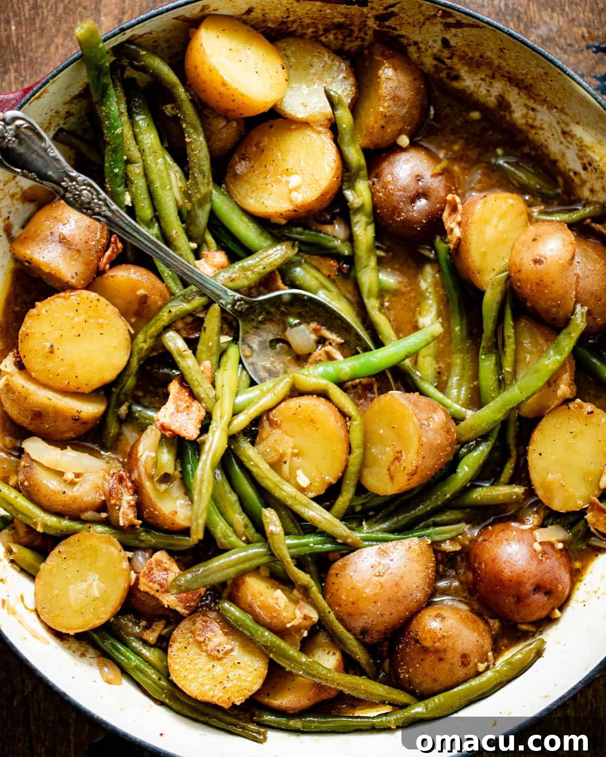 Green beans and potatoes simmering in a large pot, ready to be served, with a serving spoon resting inside.