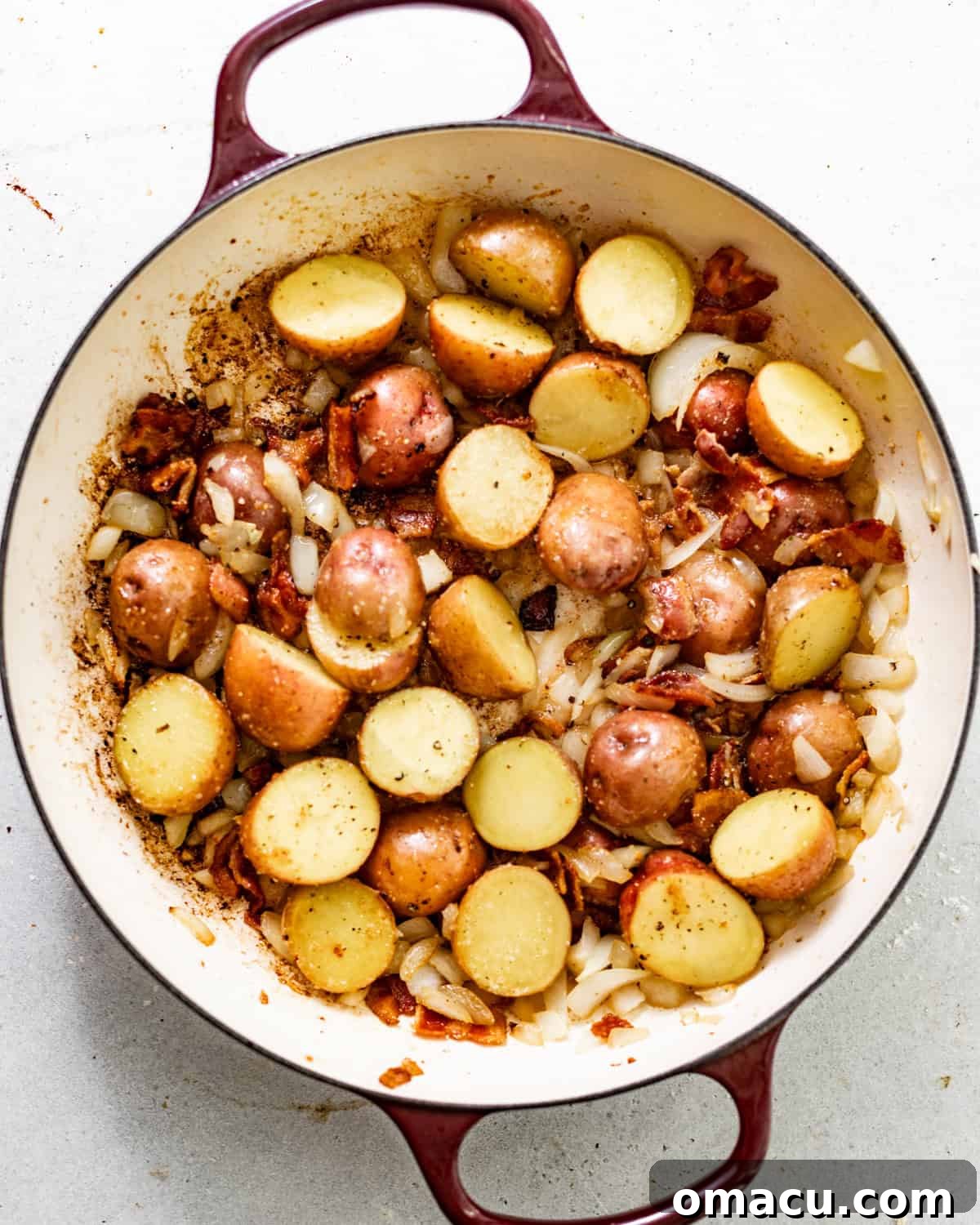 Diced potatoes, chopped onions, and a mix of seasonings cooking alongside crispy bacon in a pot.