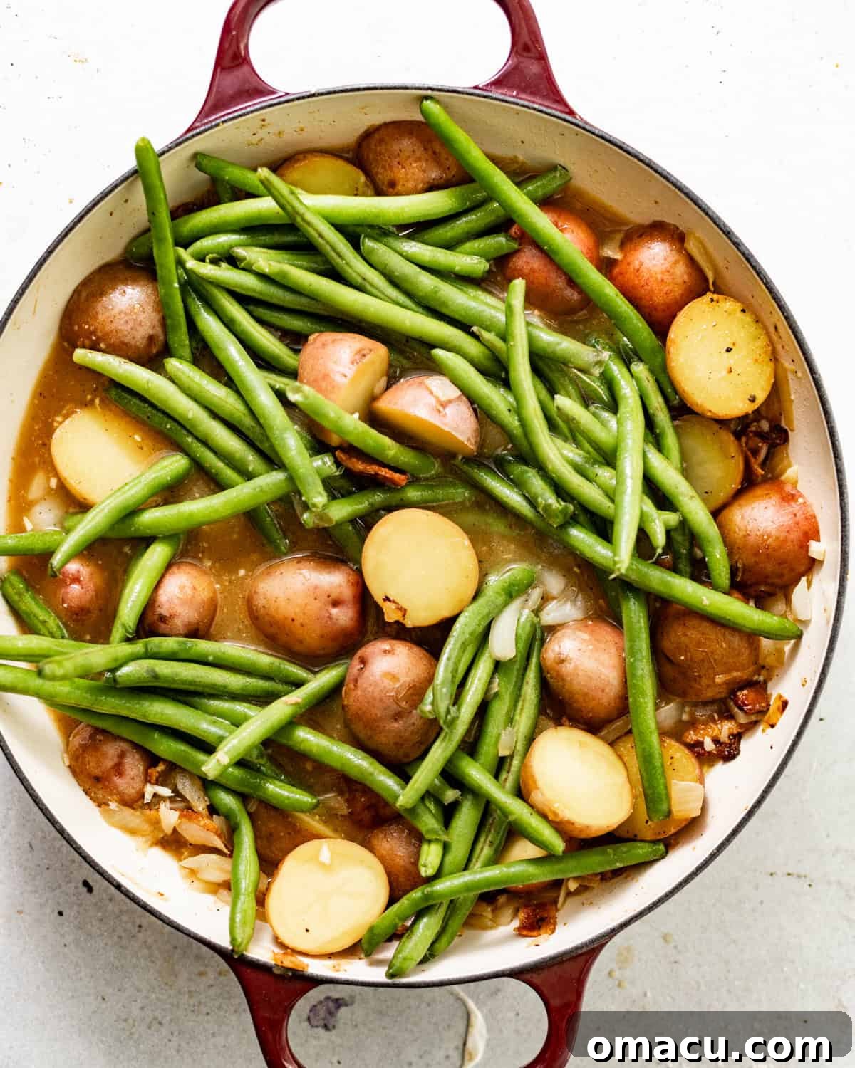 Fresh green beans and golden-brown potatoes simmering in a rich chicken broth inside a large pot.