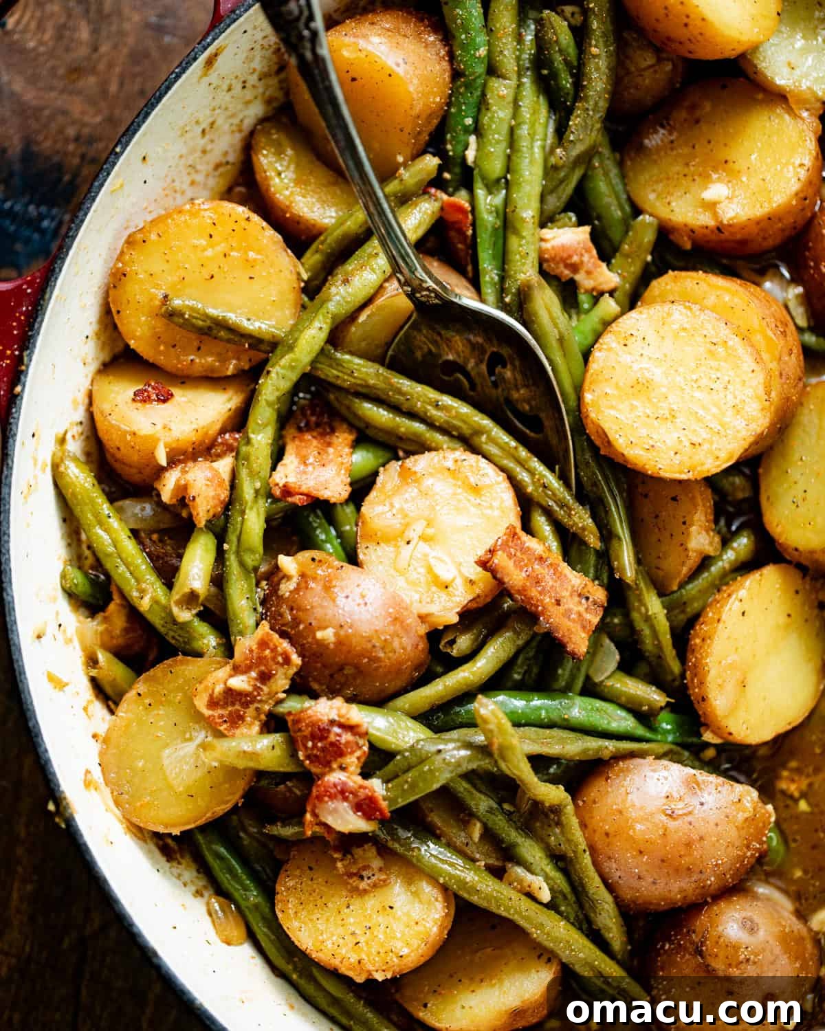 A close-up view of the tender green beans and potatoes swimming in their flavorful broth within a large pot, highlighted by a serving spoon.