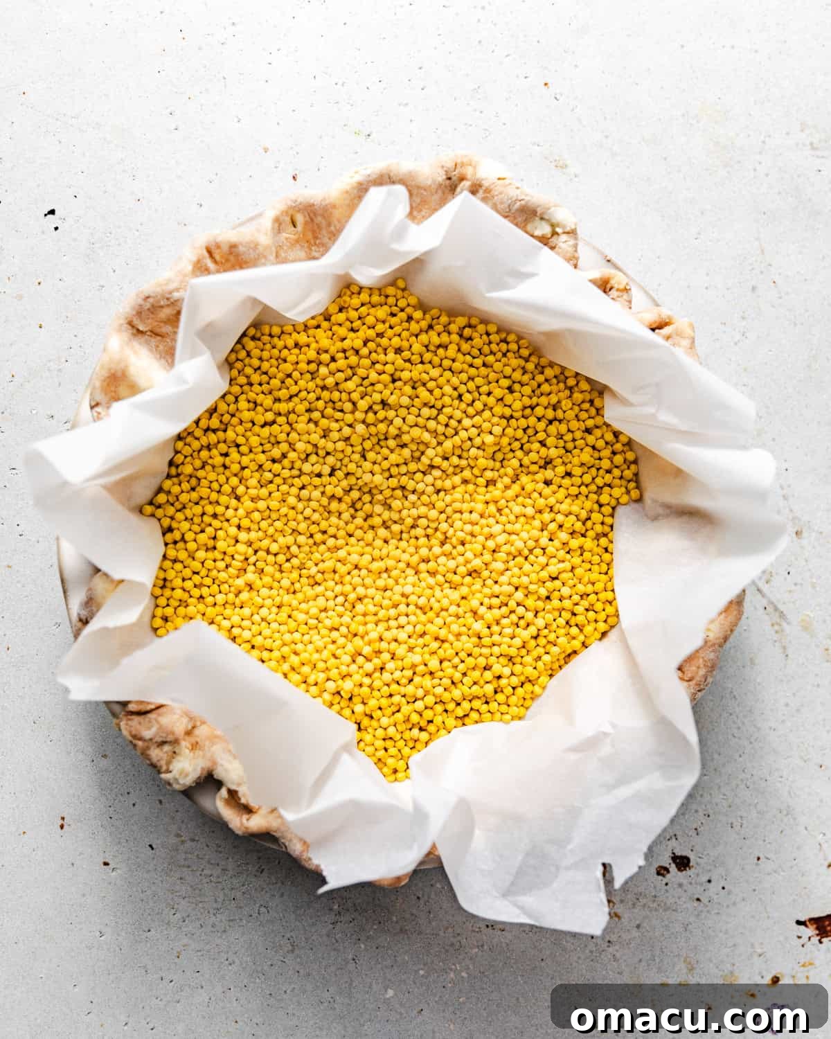 Pie crust in a pie dish, lined with parchment paper and filled with pie weights for blind baking.