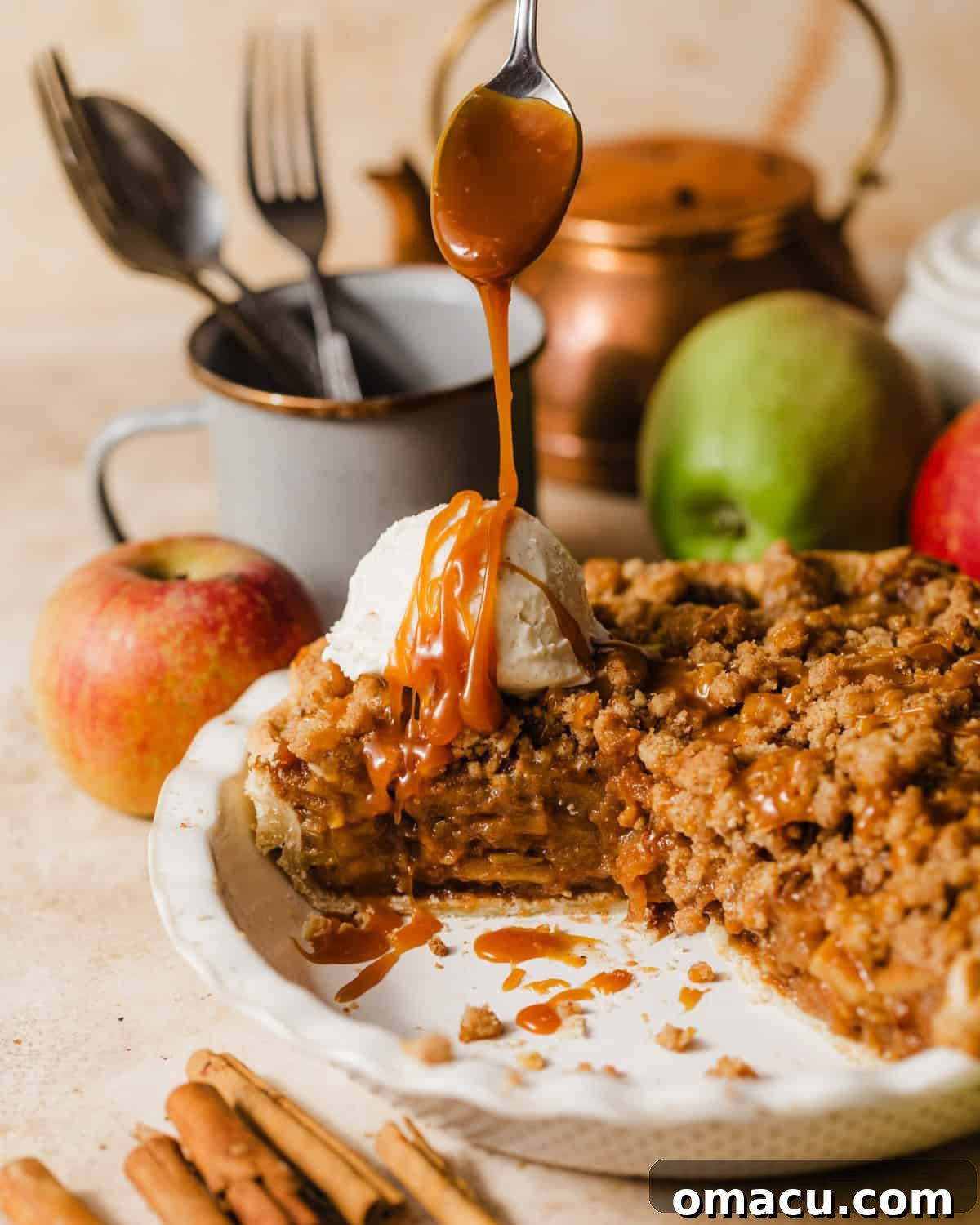 A golden-brown salted caramel Dutch apple pie fresh out of the oven in a pie dish, with a slice already removed. It's garnished with ice cream and warm salted caramel sauce being drizzled over it.