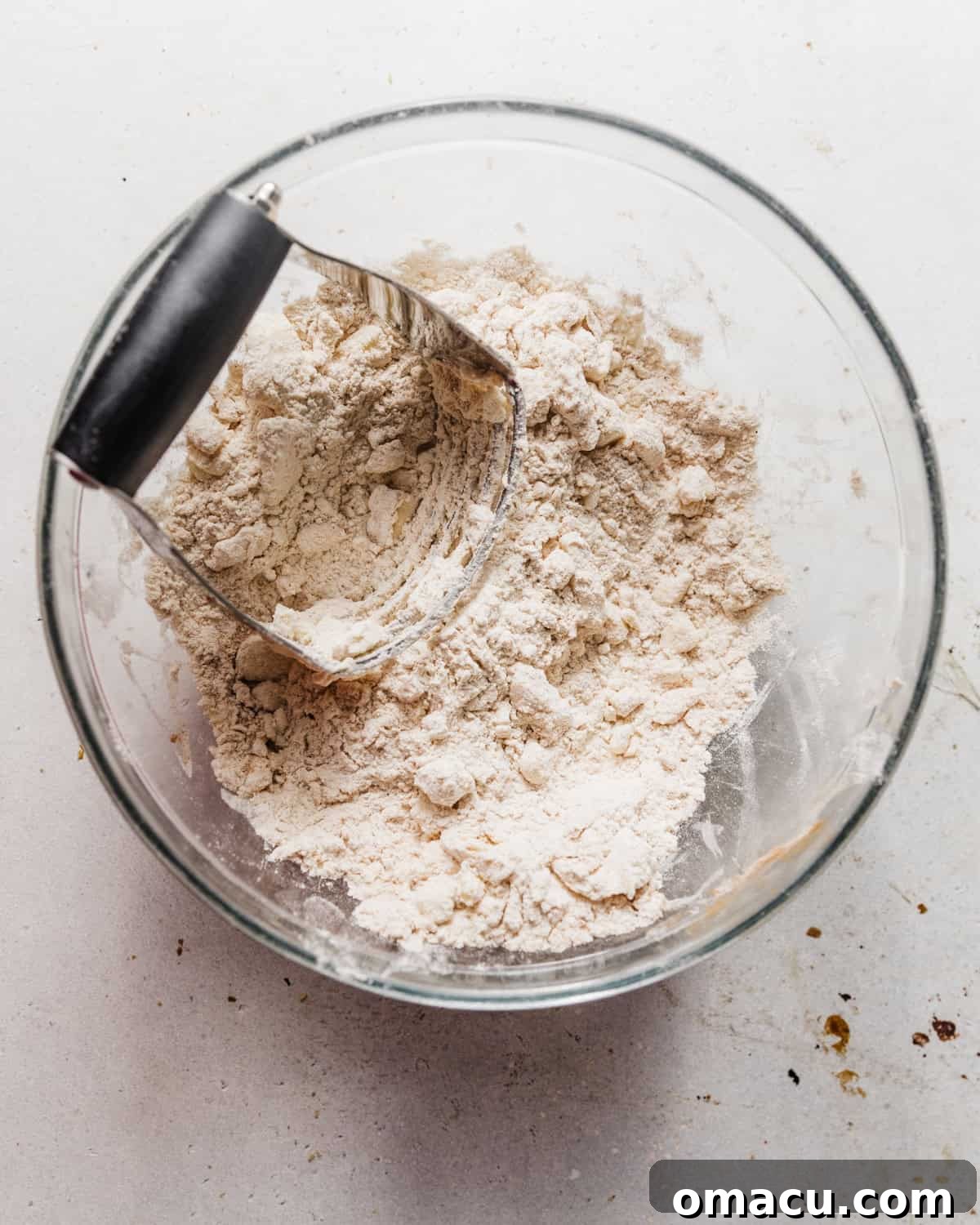 Butter and flour mixed together in a bowl using a pastry cutter, forming pea-sized morsels.