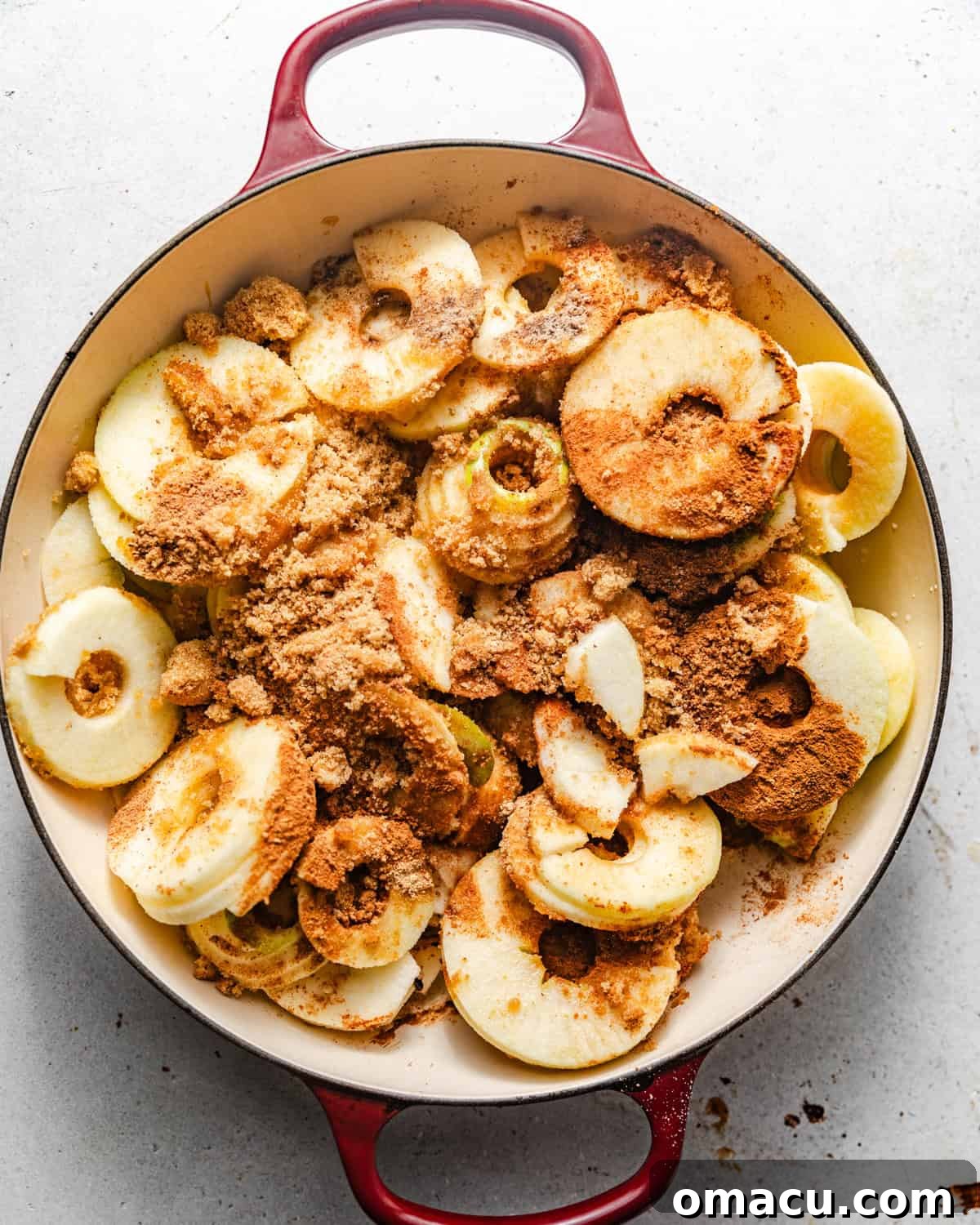 Sliced apples coated in brown sugar and warm spices in a large pan, ready to be cooked for the pie filling.