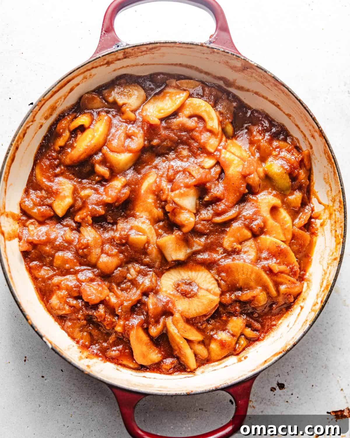 Cooked apple pie filling simmering in a large pan, with a thickened, glossy sauce.