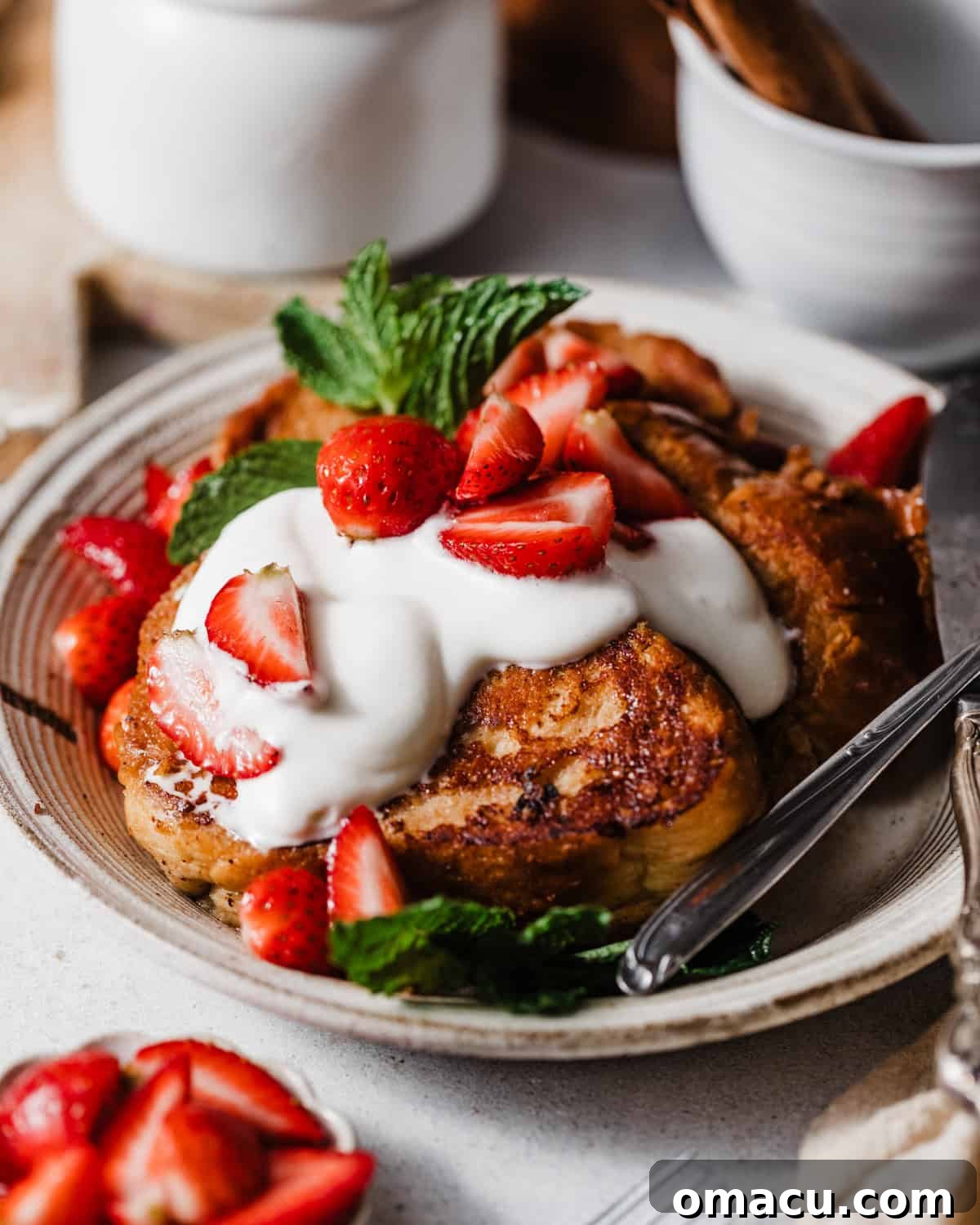 buttermilk french toast on a plate with whipped cream, maple syrup, and macerated strawberries.