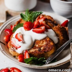 buttermilk french toast on a plate with whipped cream, maple syrup, and macerated strawberries.