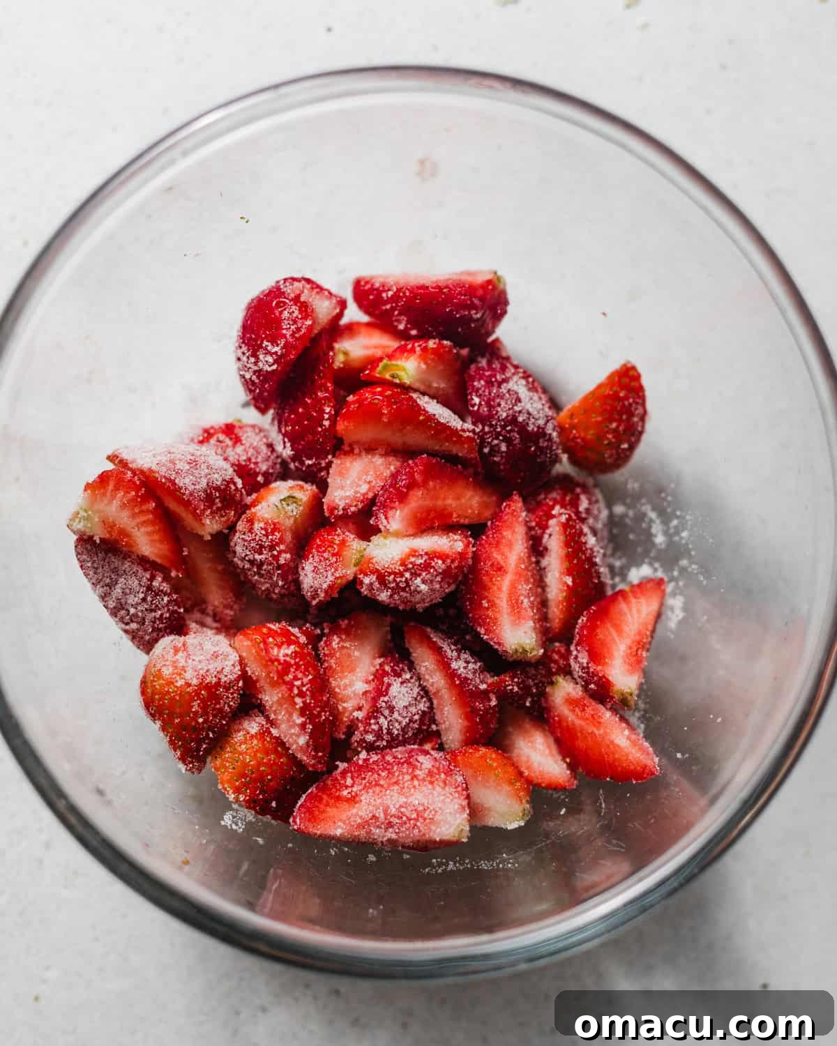 strawberries and sugar tossed together in a bowl. 