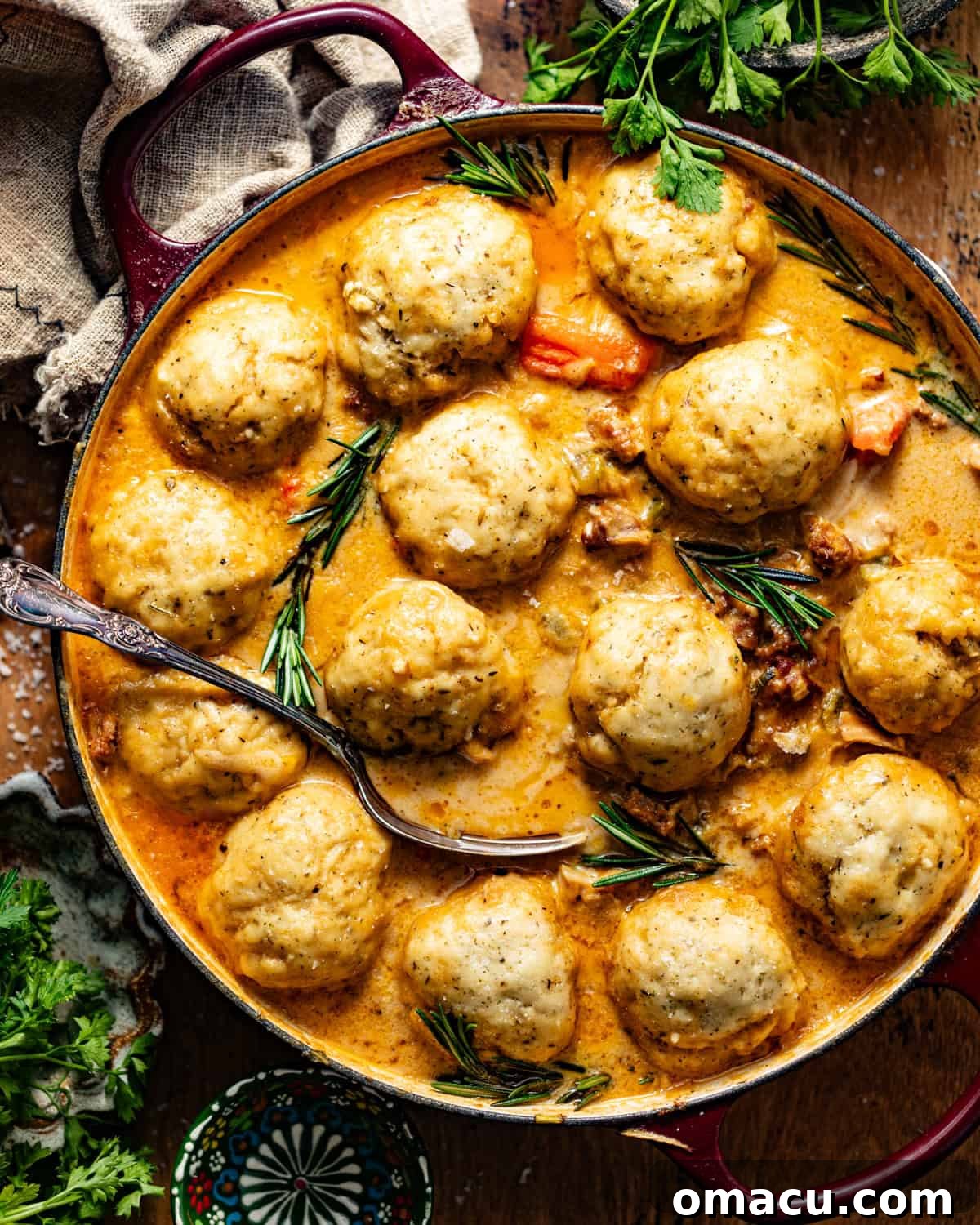 chicken and dumplings in a dutch oven with a serving spoon and fresh parsley on top.