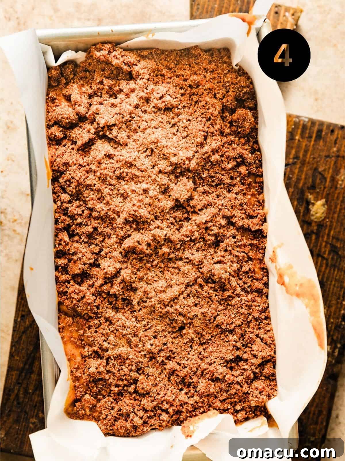 Sweet potato bread batter carefully poured into a 9x5 inch loaf pan, lined with parchment paper, and generously topped with the prepared cinnamon streusel mixture, ready for baking.