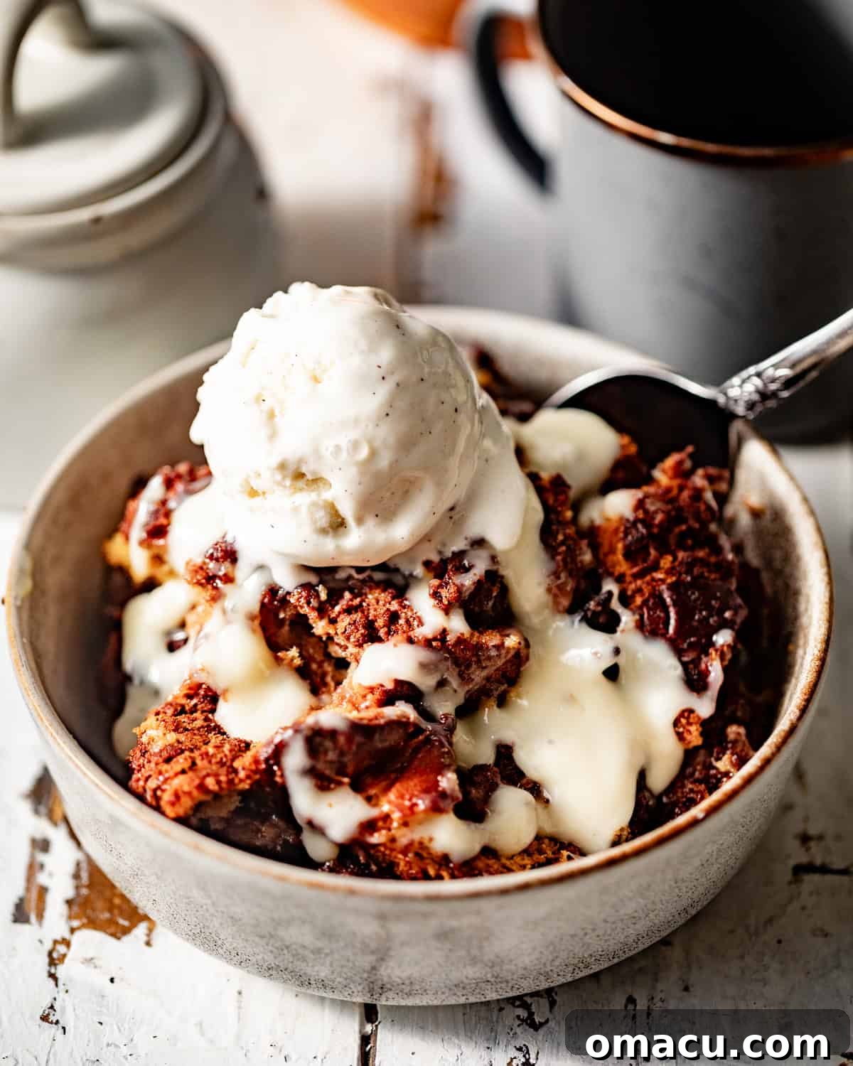 A serving of bread pudding in a bowl, generously drizzled with vanilla sauce and topped with a scoop of melting ice cream.