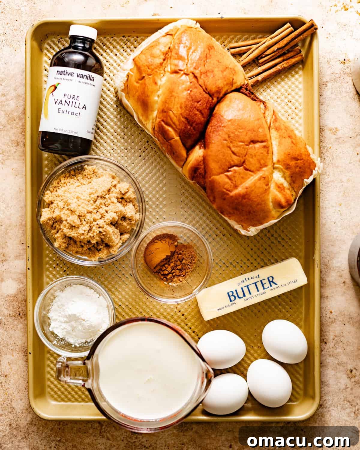 Ingredients laid out for making bread pudding: brioche bread, vanilla extract, brown sugar, cinnamon, eggs, butter, milk, and kosher salt.