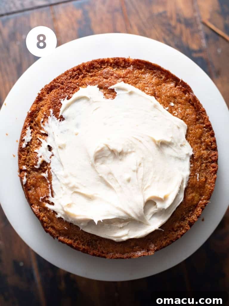 Layered carrot cake on a cake stand, with its first generous layer of cream cheese frosting.