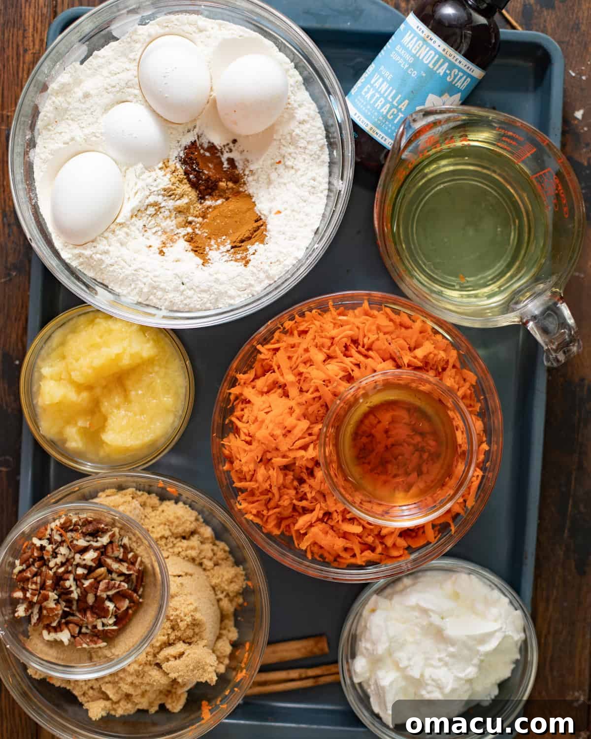 All the fresh ingredients for homemade carrot cake laid out on a baking sheet, including carrots, pineapple, spices, and butter.