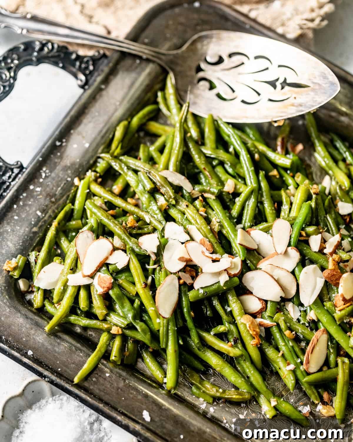 Crispy garlic butter roasted frozen green beans on a serving tray topped with fresh garlic and toasted sliced almonds.