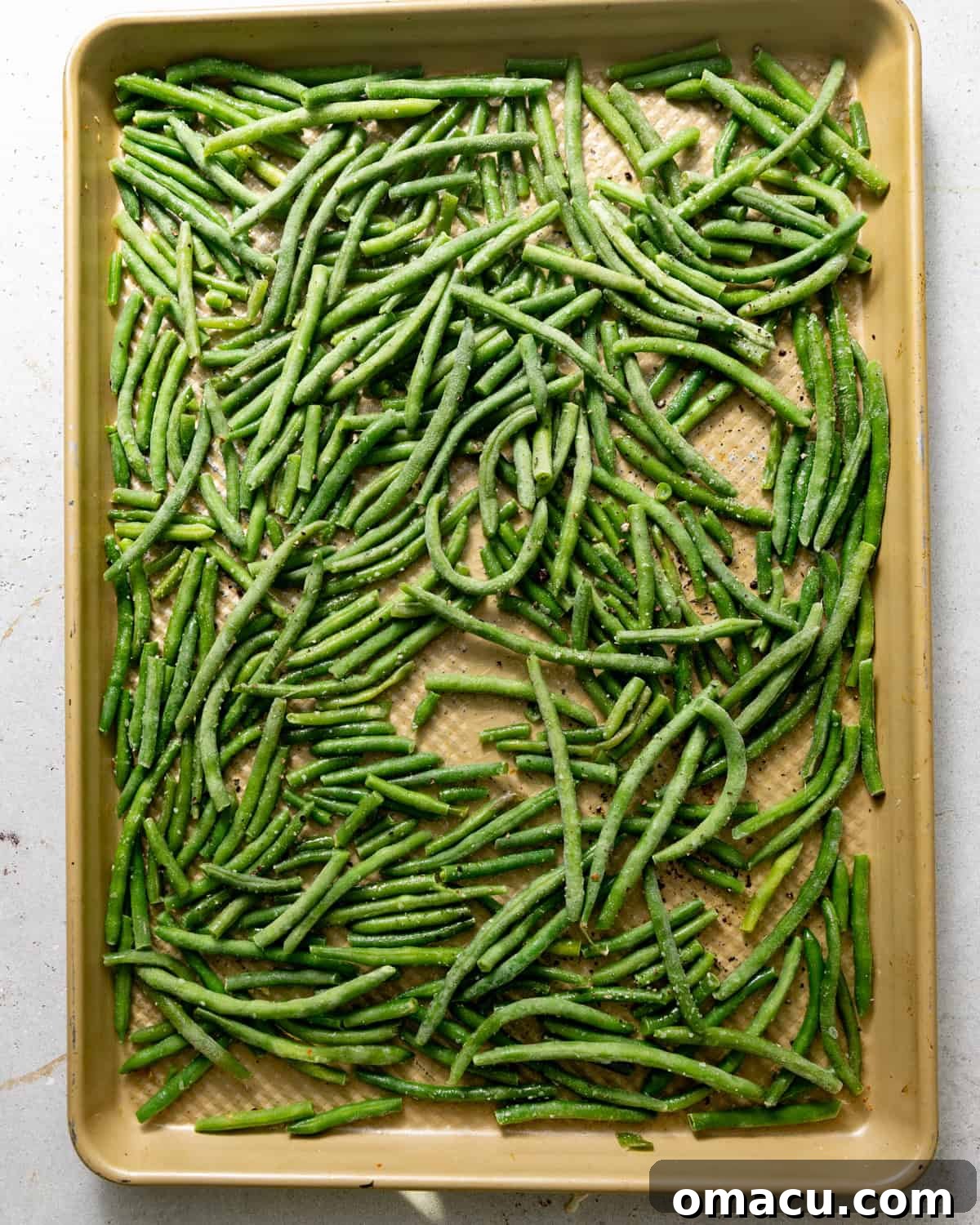 Frozen green beans spread in a single layer on a parchment-lined baking sheet.