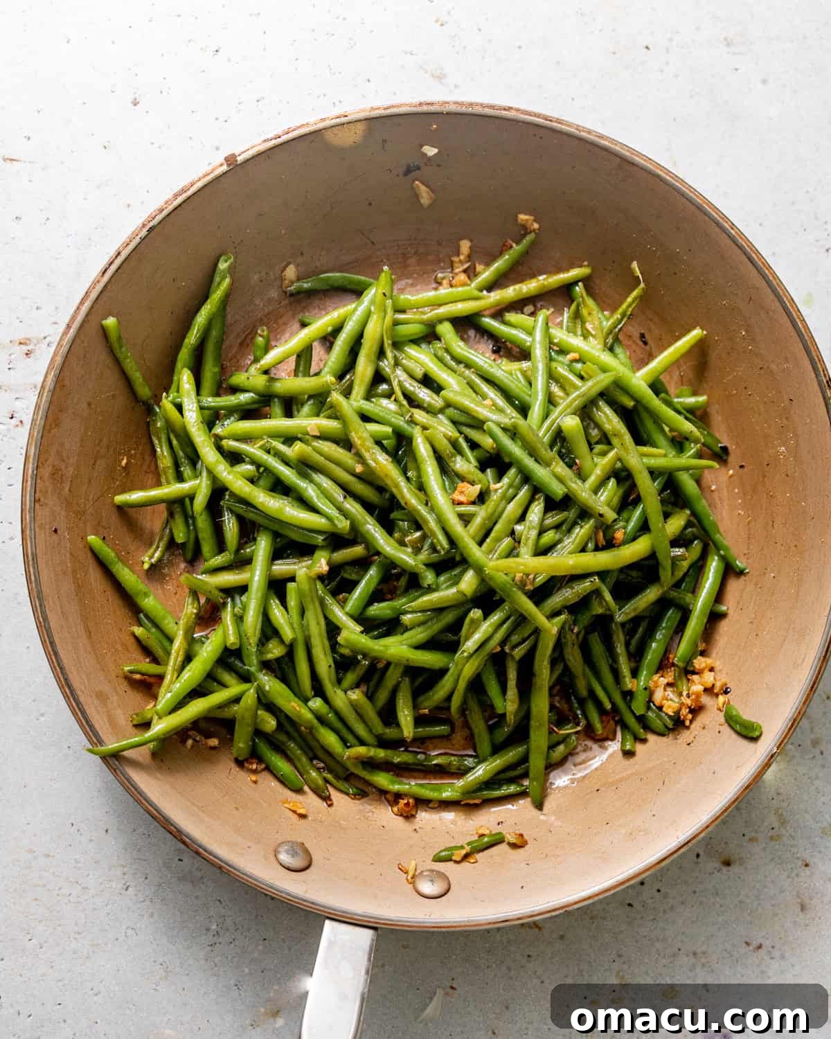Roasted green beans freshly tossed in the garlic butter mixture in a bowl.