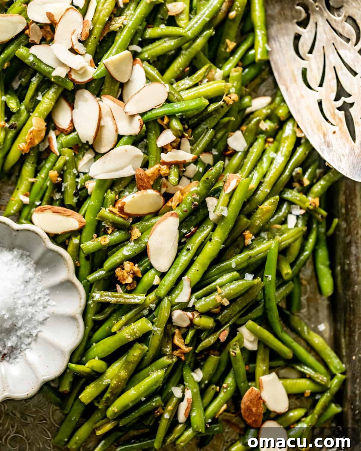 Roasted green beans ready to serve on a plate, garnished with sliced almonds and a sprinkle of flaky sea salt.