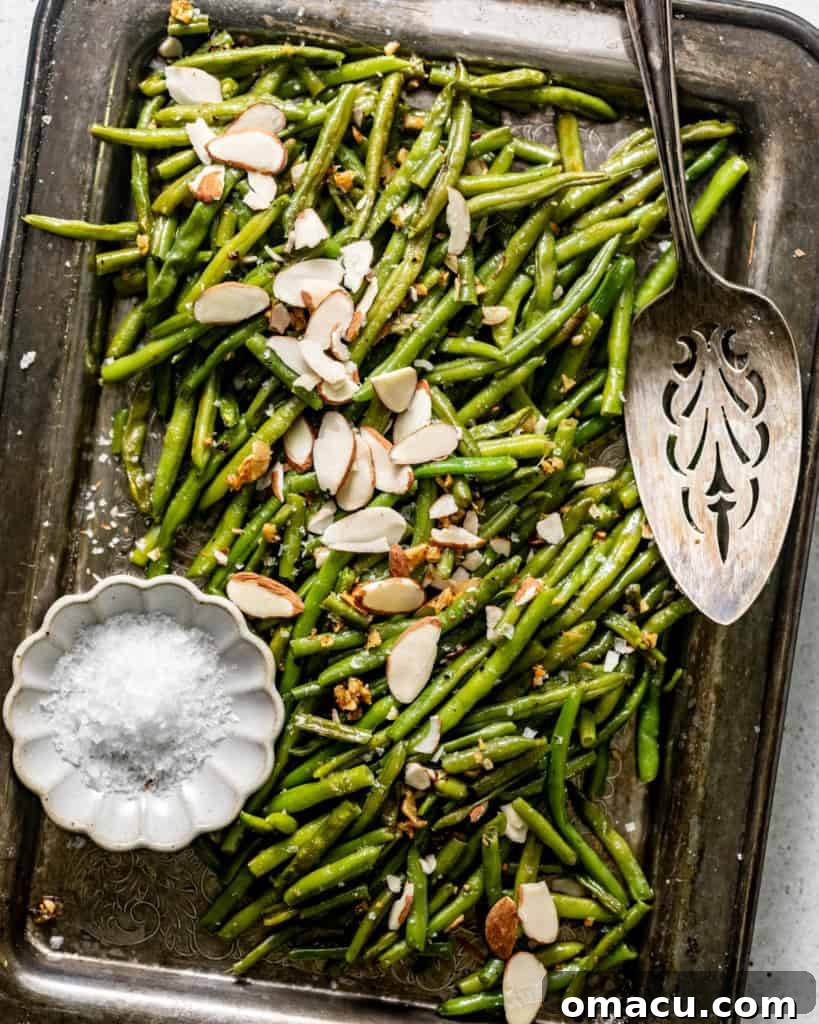 Frozen roasted green beans topped with sliced almonds on a serving tray with a serving spoon, ready for a holiday meal.