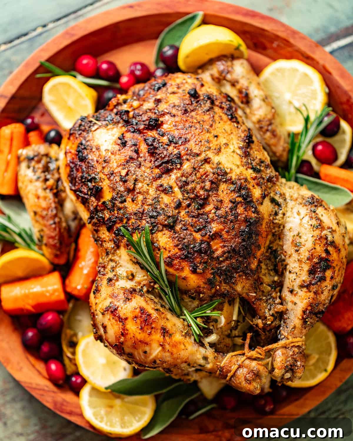 a whole roasted chicken on a serving tray with veggies, cranberries, lemon, and herbs.