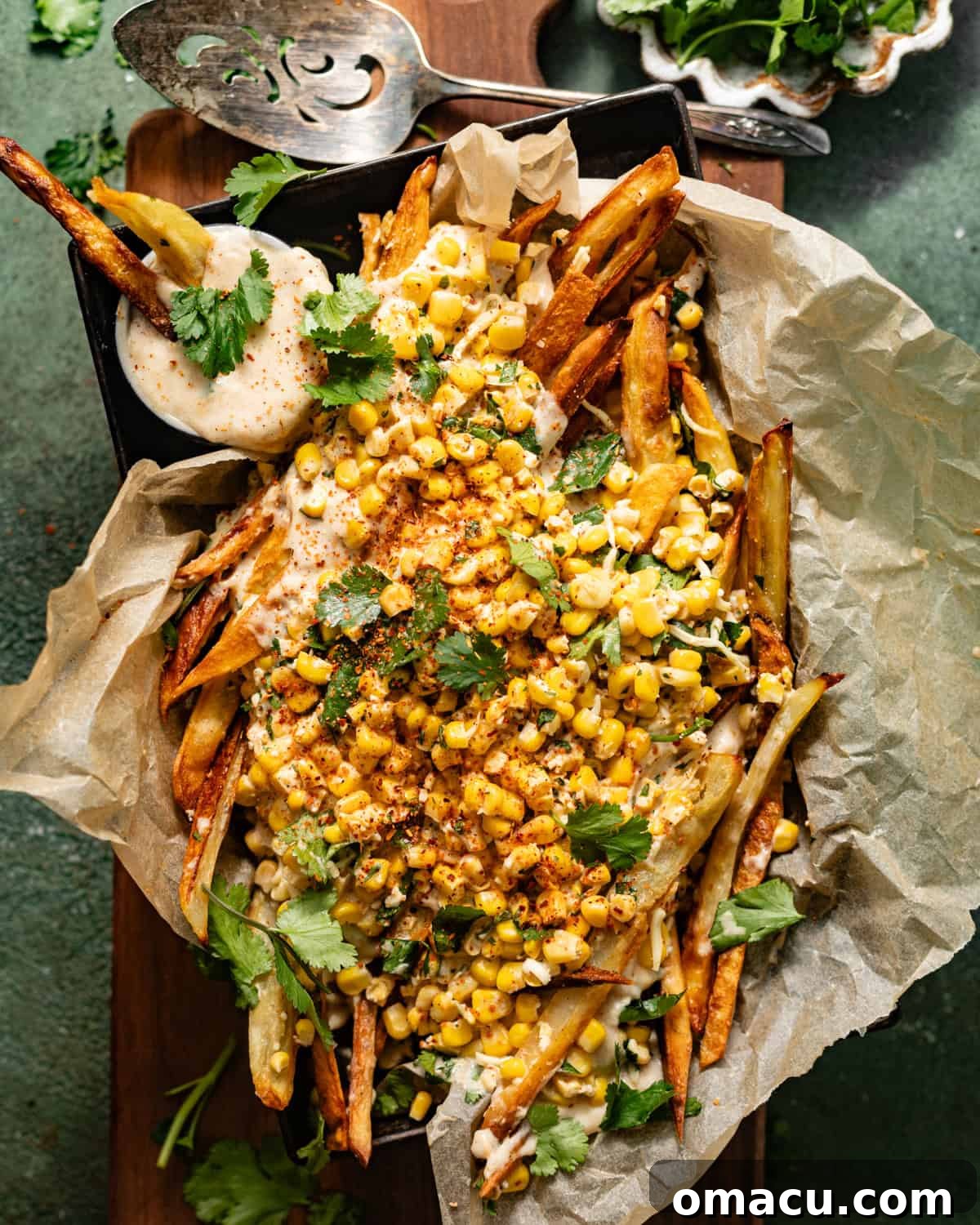 Elotes fries in a serving tray topped with queso, cilantro, cotija, and corn, ready to be enjoyed.