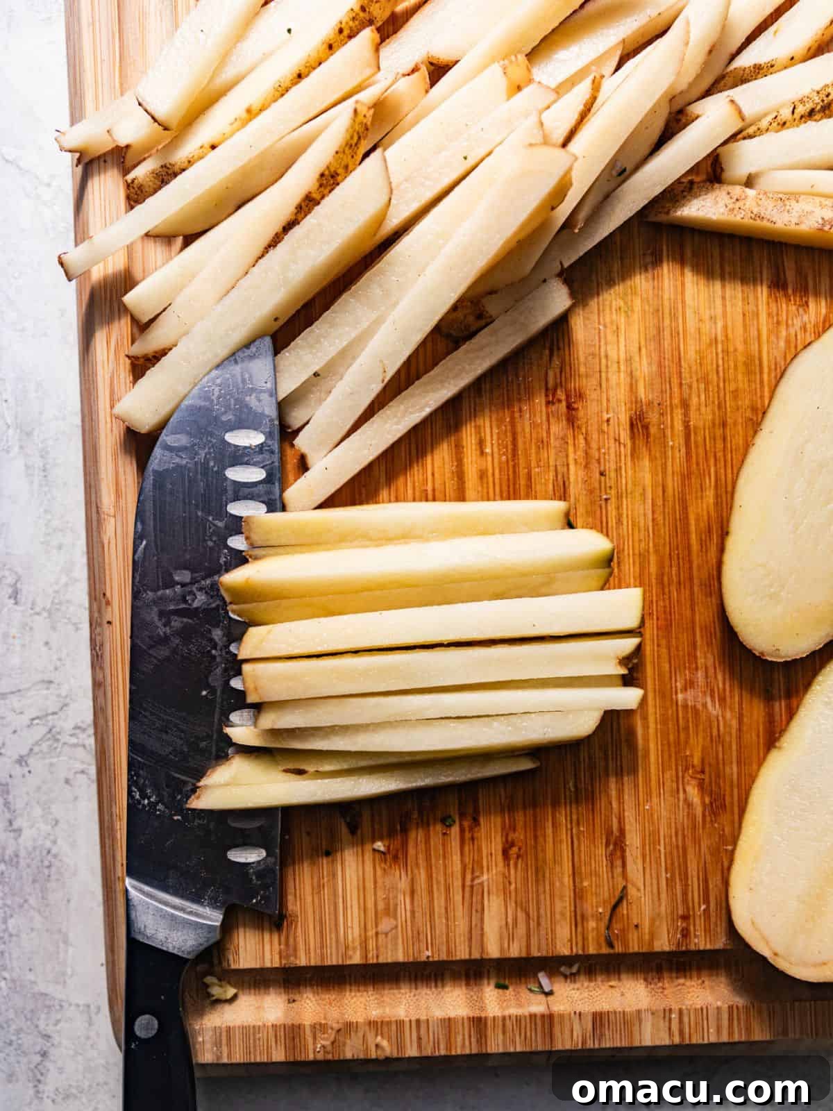 Raw potatoes cut into uniform french fry shapes on a cutting board, ready for soaking.