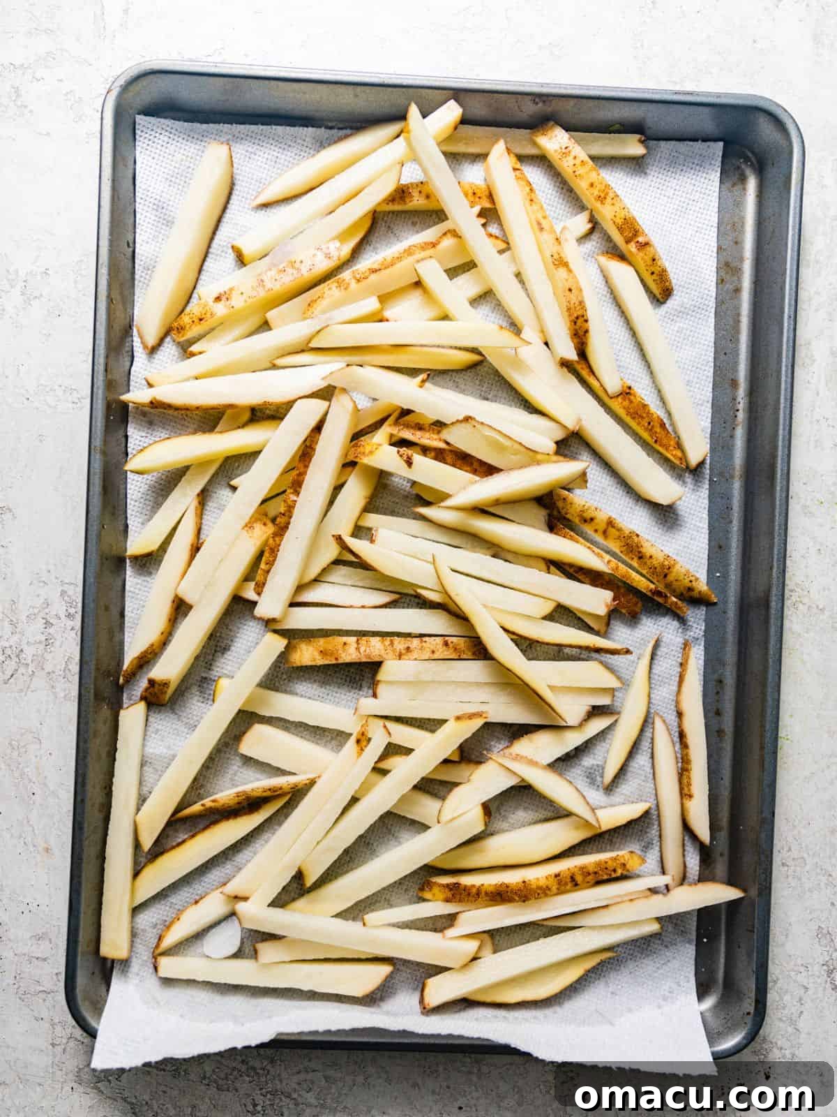 Seasoned and prepared raw french fries laid out on a parchment-lined baking sheet.
