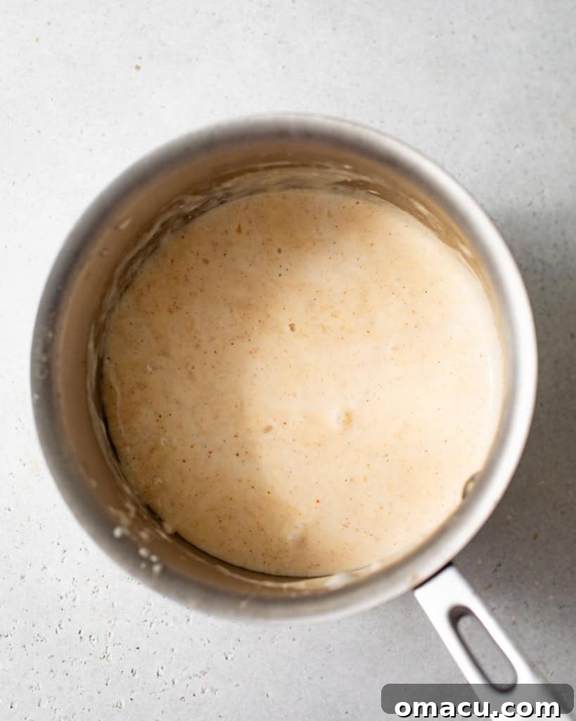 Creamy, melted queso sauce simmering in a small saucepan on the stove.