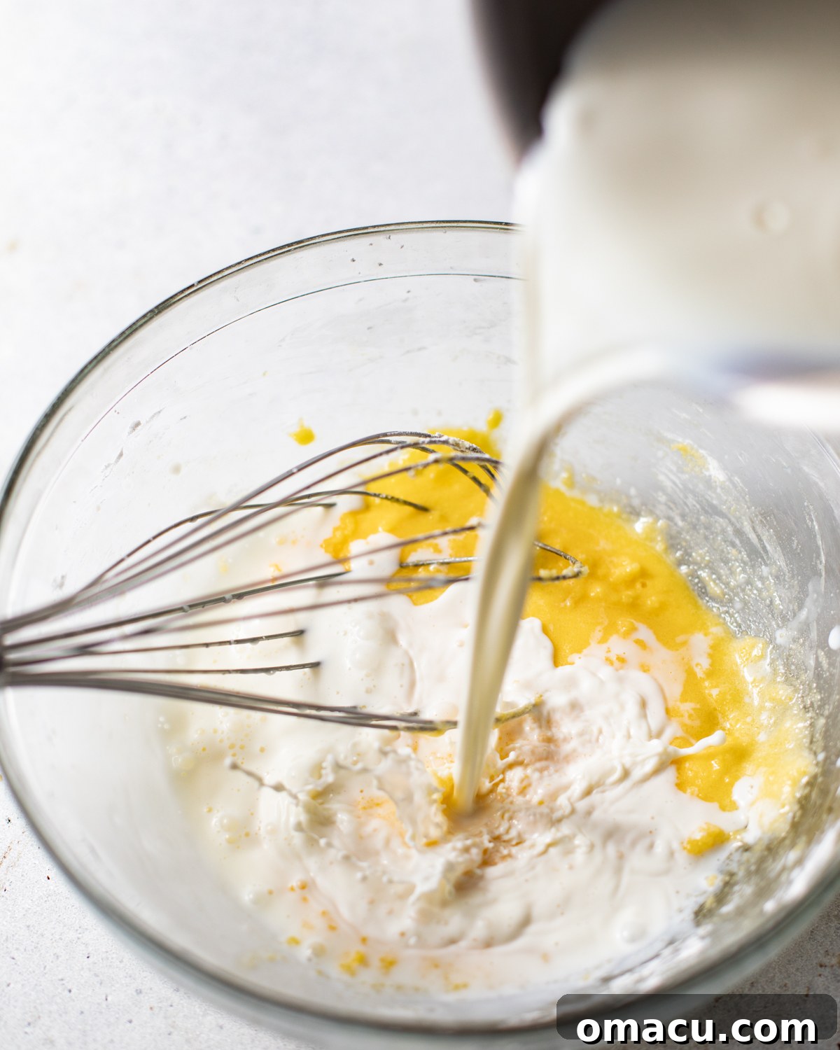 egg yolks whisked together in a bowl with warm milk being poured into it to make the pastry cream topping.