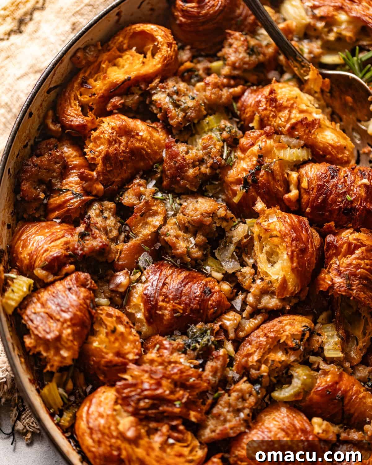 A golden-brown croissant stuffing in a circular baking dish, garnished with fresh herbs, ready for serving at a holiday feast.