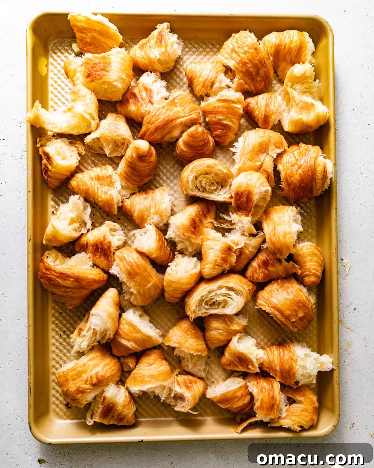 Torn croissant pieces spread evenly on a baking sheet, toasted to a light golden brown, preparing for the stuffing mixture.