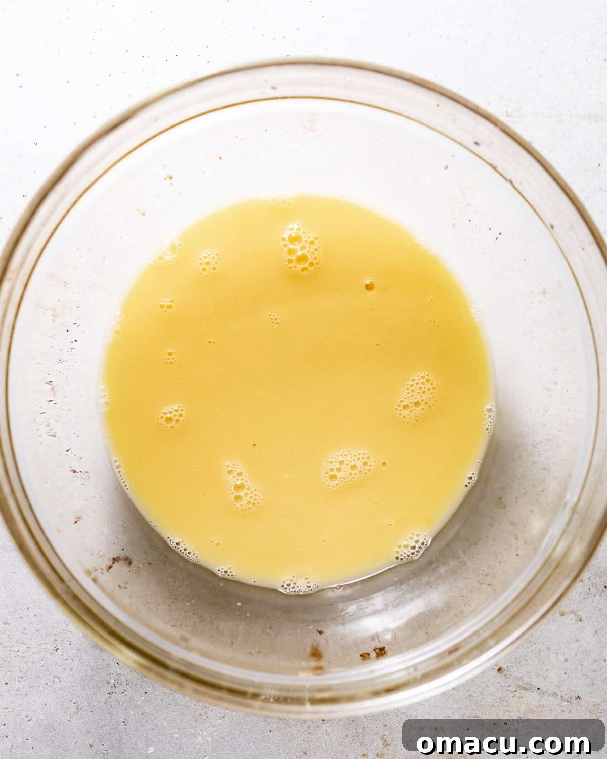 Three large eggs, lightly whisked together in a mixing bowl, creating a smooth, pale yellow liquid custard base.