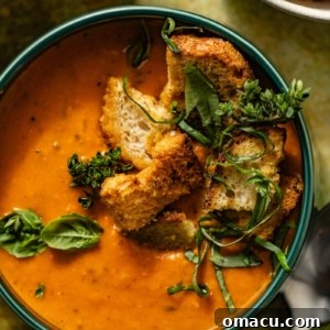 Heirloom tomato soup in a bowl with fresh herbs, croutons, and spoons